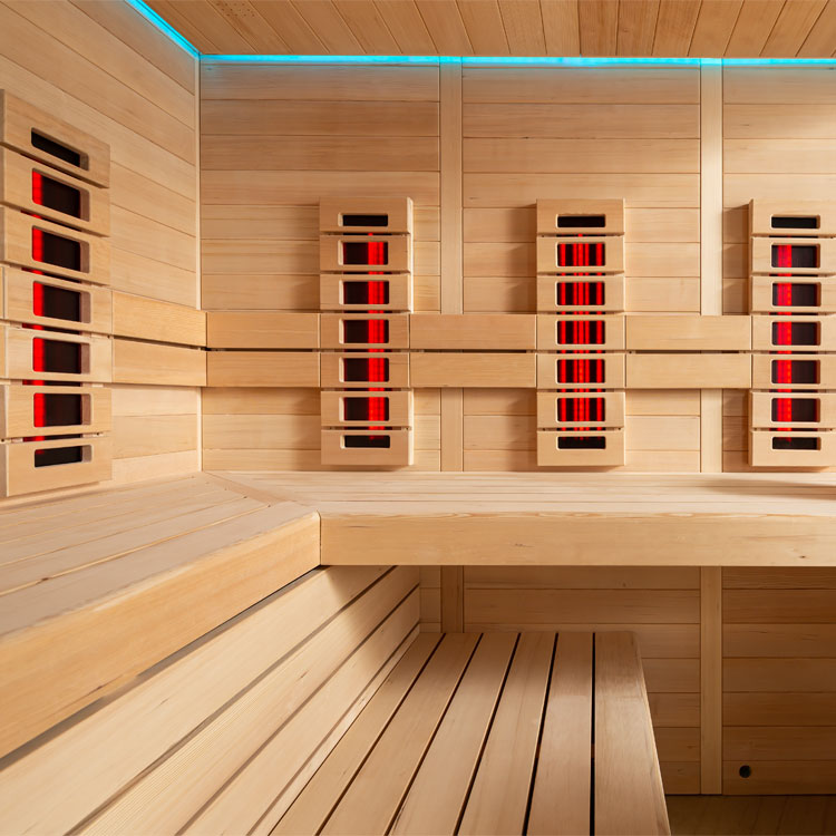 Holzsauna Innenansicht mit Bänken, IR-Strahlern, Eimer und Schöpfkelle. Weiche Beleuchtung und Sanduhr an der Wand.
